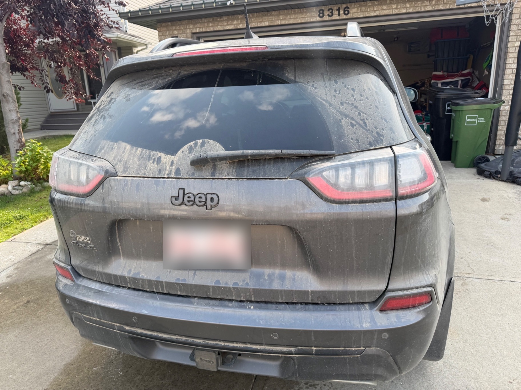 Muddy rear of a grey Jeep Cherokee before detailing